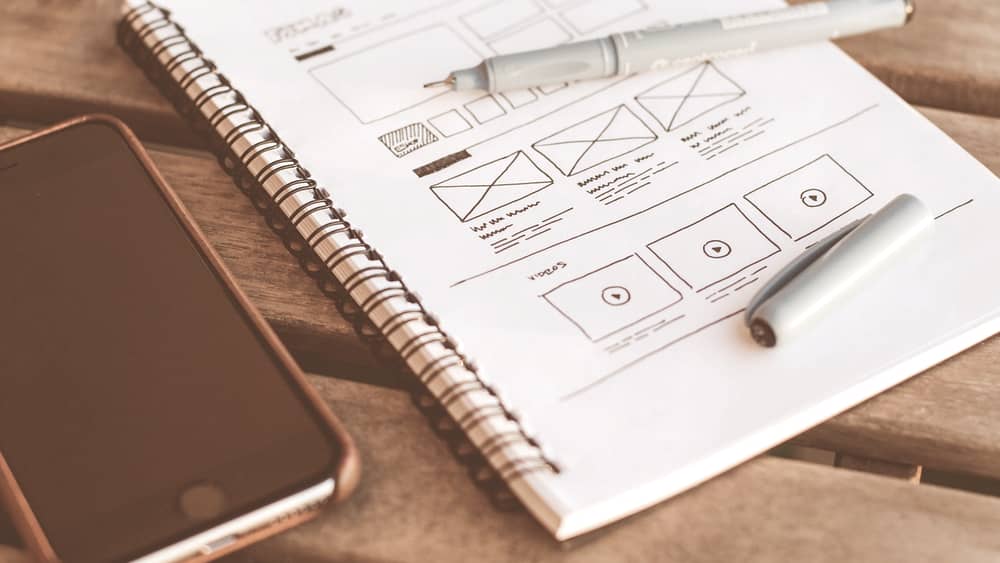 Notebook with hand-drawn interface wireframes beside a phone