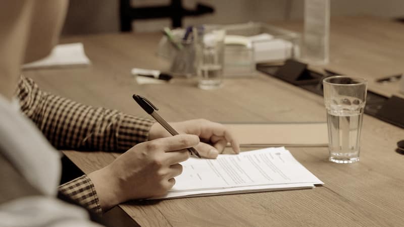 Hands signing printed documents at a desk
