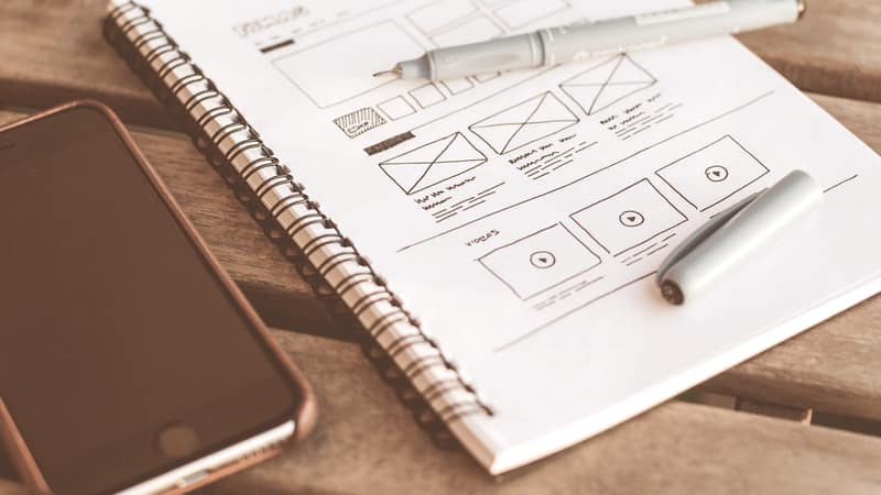 Notebook of hand-drawn interface wireframes beside a phone